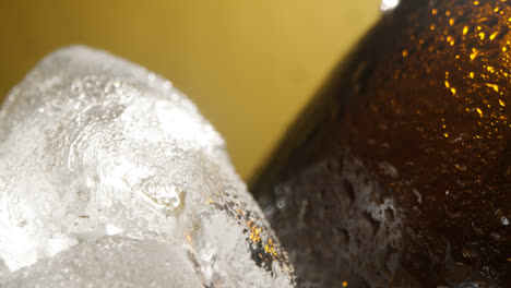 Nahaufnahme-Von-Kondensationstropfen,-Die-An-Glasflaschen-Mit-Kaltem-Bier-Oder-Erfrischungsgetränk-Herunterlaufen-Und-In-Einem-Mit-Eis-Gefüllten-Eimer-Vor-Gelbem-Hintergrund-Abkühlen-2
